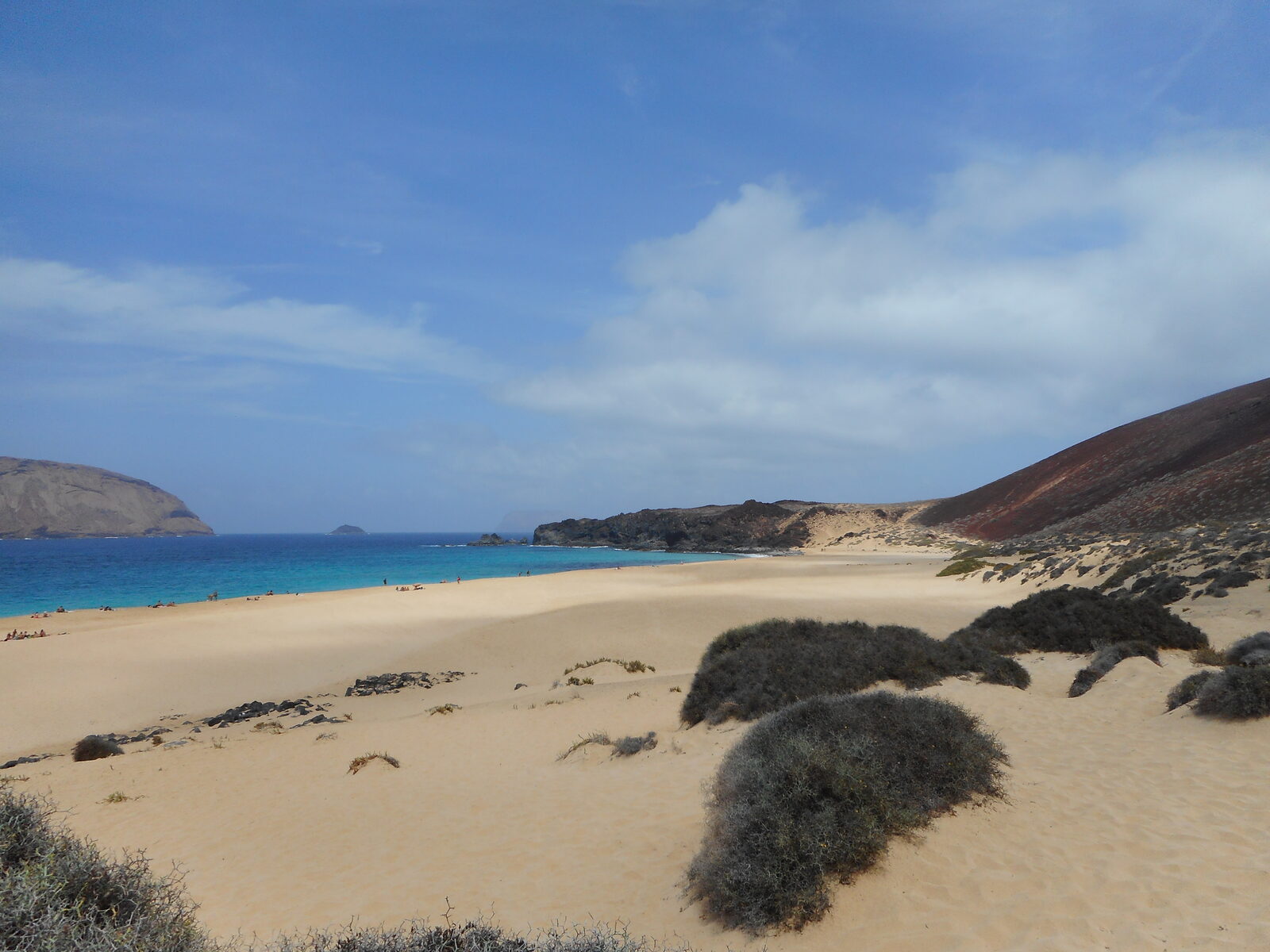 Playa de las Conchas en la costa norte de La Graciosa, arena clara enmarcada por el cono volcánico rojo de Montaña Bermeja