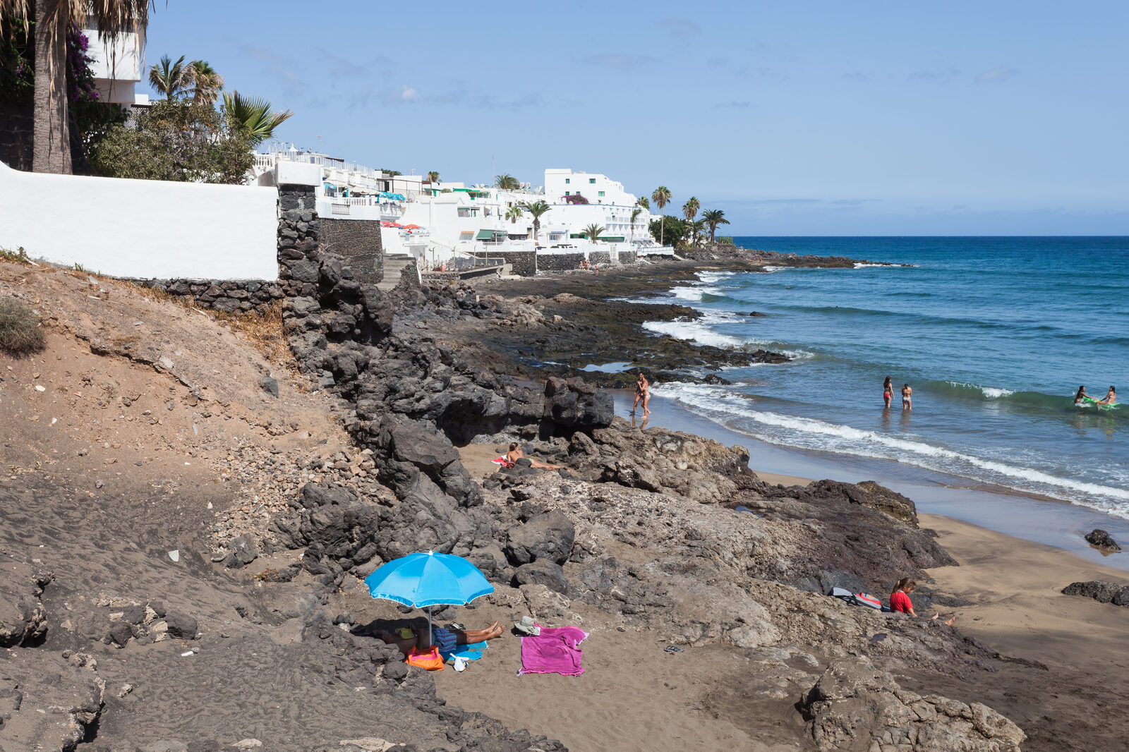 Playa Grande en Puerto del Carmen, Lanzarote, con hamacas y sombrillas sobre arena oscura y agua transparente