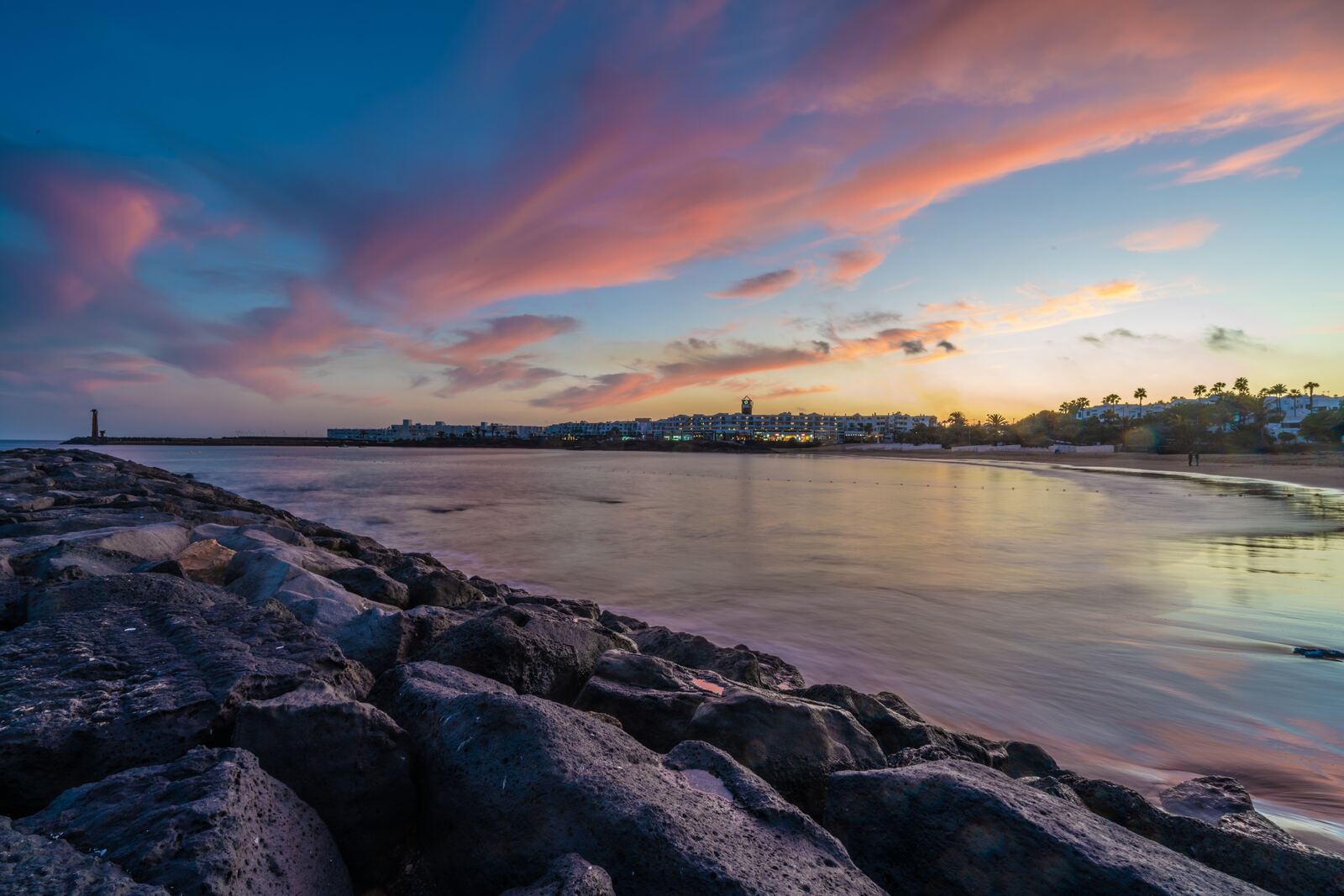 Sonnenuntergang über der Bucht von Costa Teguise im Sommer mit der Skyline des Ortes und dem Felsenwellenbrecher, Lanzarote