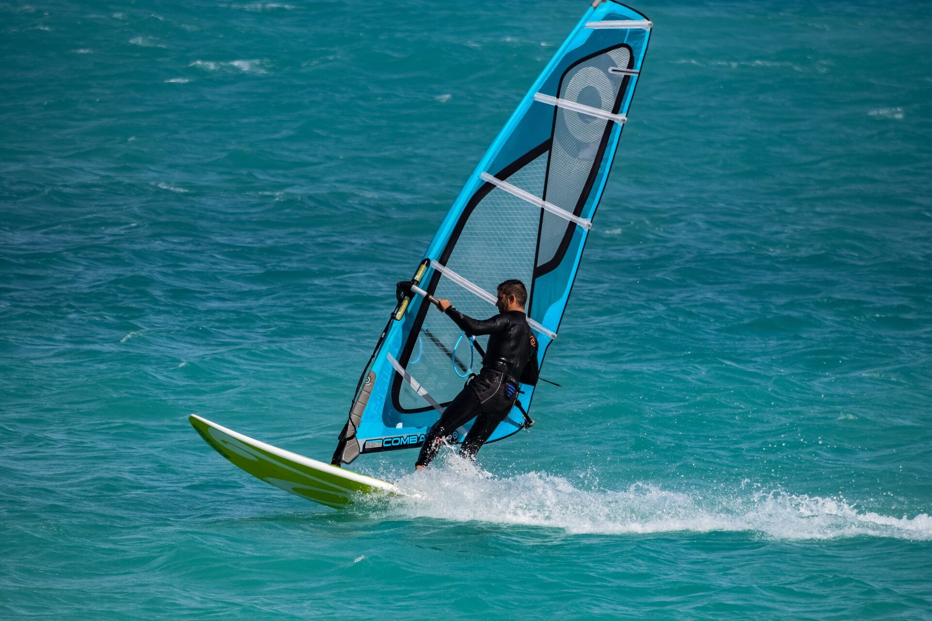 Windsurfista en una tabla turquesa cortando el agua bajo una vela azul