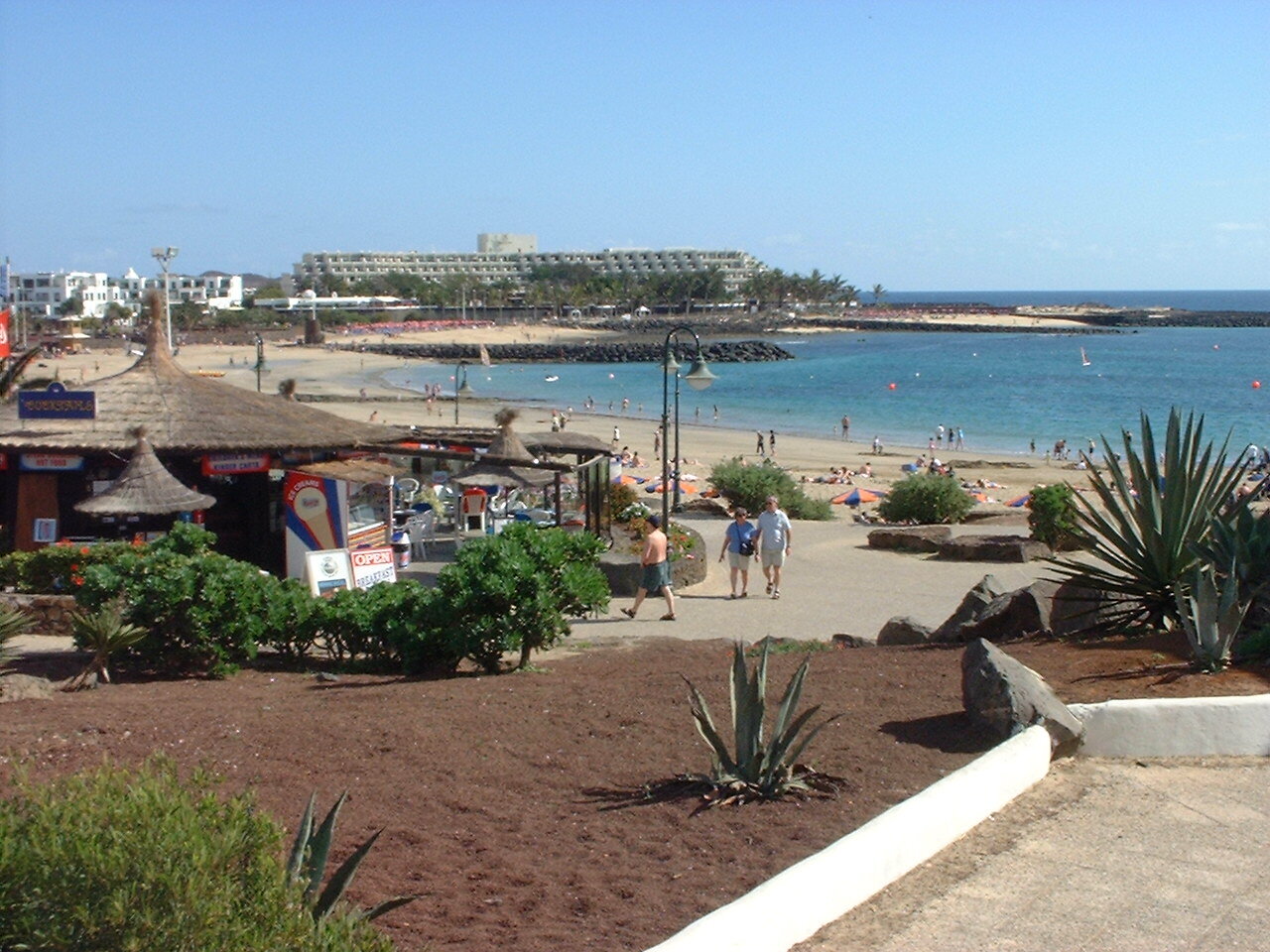 Playa Las Cucharas en Costa Teguise concurrida, con sombrillas naranjas y azules y bañistas