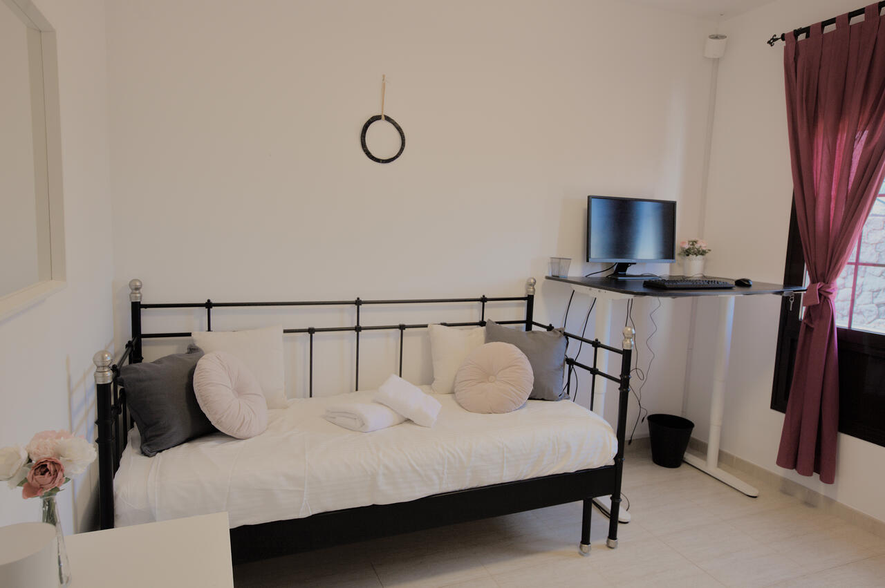 Studio bedroom at Casa Los Alisios with a motorised sit-stand desk in standing position, ergonomic chair and a wrought-iron daybed. Costa Teguise, Lanzarote.