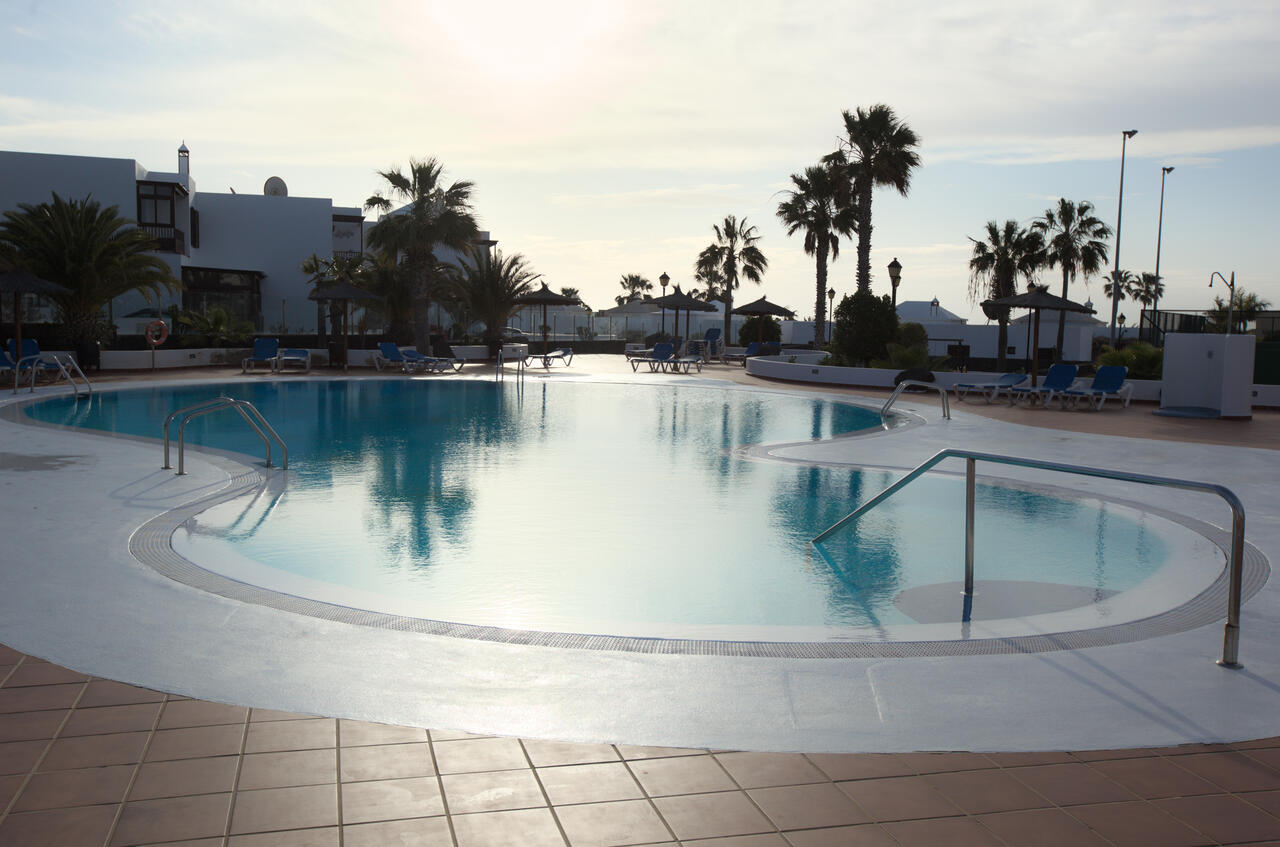 Gemeinschaftspool mit Palmen in der Anlage von Casa Los Alisios bei Sonnenuntergang, Costa Teguise, Lanzarote
